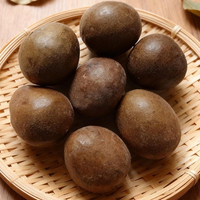 May include: A close-up shot of seven brown, oval-shaped lo han guo fruits arranged in a woven bamboo basket. The fruits have a slightly textured surface and are a rich, dark brown color. The basket is light brown.