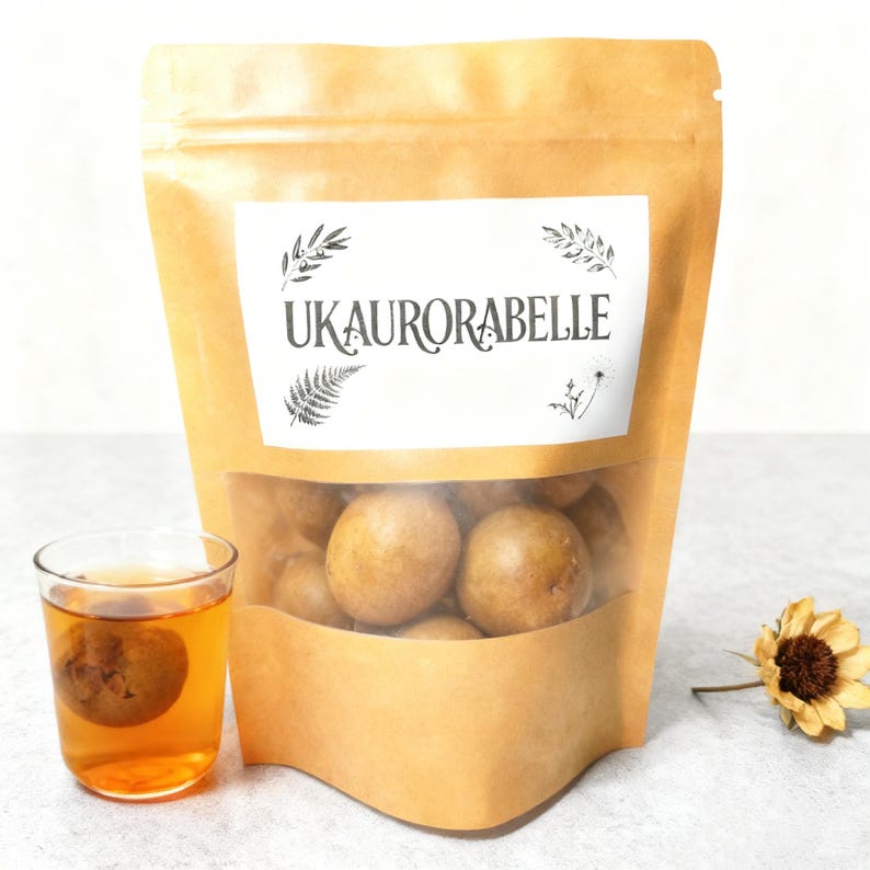 May include: A brown paper bag with a clear window containing several round, light brown food items. A glass of amber-colored liquid with a round item inside sits to the left. The bag has a white label with the text "UKAURORABELLE".