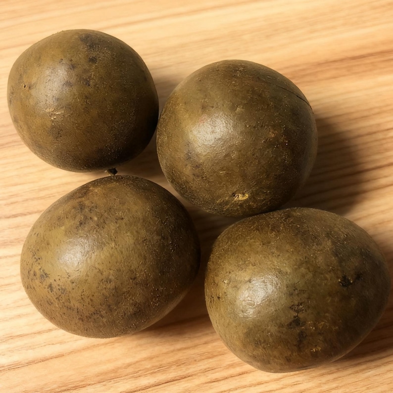 May include: Four round, brown fruits with a slightly textured surface are arranged on a light-colored wooden surface. The fruits have a dark brown hue and a smooth, spherical shape. The image is well-lit, highlighting the natural tones of the fruits.