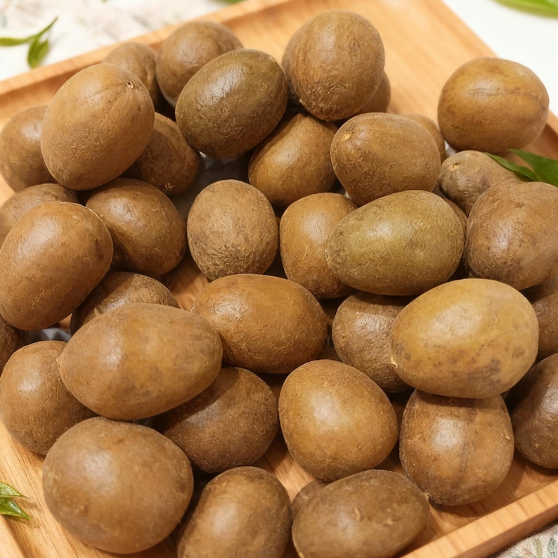 May include: A wooden tray filled with numerous brown, oval-shaped fruits. The fruits have a smooth skin and vary slightly in color, ranging from light to dark brown. The arrangement suggests a harvest or display of fresh produce.