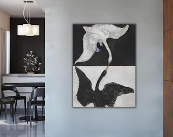 Op de afbeelding: Een canvas print met een zwart-wit schilderij van twee zwanen. De ene zwaan is wit met gespreide vleugels, de andere zwart met gespreide vleugels. De zwanen staan tegenover elkaar, hun snavels raken elkaar bijna aan.