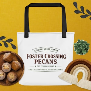 以下が含まれることがあります： 黒い持ち手が付いた白いトートバッグ。茶色で「FOSTER CROSSING PECANS」の文字、さらに「EST TEXAS ORCHARD」と「500 TREES OF GOOD OLD-FASHIONED FUN」の文字がプリントされています。黄色い背景に配置されています。