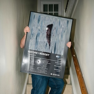 Op de afbeelding: Een ingelijste poster getiteld Before I Forget van The Kid LAROI, met een fotografisch portret van een persoon die gedeeltelijk onder water is. De zwarte lijst toont een tracklist van 24 nummers, releasedatum 24 april 2026 en albumduur 70:37.