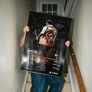 May include: A framed rectangular poster featuring the album cover for Last Lap by Rod Wave. The artwork displays a person in a tan shirt with a graphic print, a tracklist of 23 songs, release date October 11, 2024, and a Spotify code at the bottom.