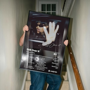 May include: A rectangular black framed poster featuring the album cover for Still Over It by Summer Walker. The artwork displays a person in sunglasses with a hand raised, alongside a tracklist, release date, and album length details.