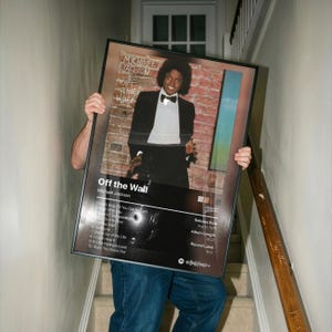 May include: A framed poster of Michael Jackson's "Off the Wall" album cover. The poster includes the album title, tracklist, release date, and record label. The image shows Jackson in a black suit and bow tie.