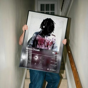 May include: A framed poster with the text "More Chaos" by Ken Carson. The artwork features a person with black dreadlocks and a shirt with red splatter. The poster includes a tracklist, release date, and album length.