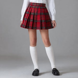 May include: A red plaid pleated skirt with green and black accents. The skirt is paired with a white collared shirt, white knee-high socks, and black loafers. The skirt's pattern is a classic tartan design.