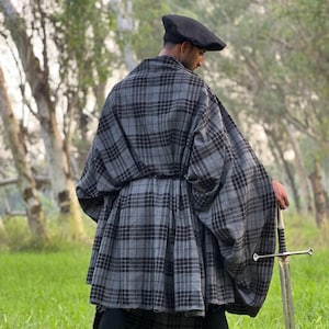 Może przedstawiać: Szary i czarny płaszcz w kratę i kilt są noszone z czarnymi legginsami i czarnym beretem. Długi srebrny miecz trzymany jest w prawej ręce. Strój jest noszony na zewnątrz na trawiastym polu.