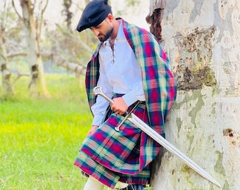 Peut inclure: Une personne vêtue d'un costume écossais traditionnel, comprenant un kilt à carreaux, un châle assorti, une chemise blanche, un béret noir et des bottes noires. L'ensemble est accessoirisé d'une longue épée. Le kilt présente un motif à carreaux rouge, vert et bleu.