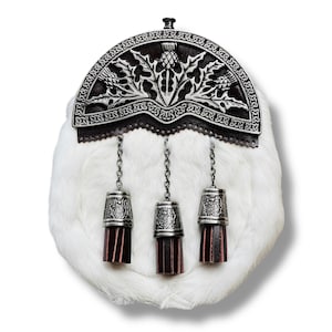 May include: A white fur sporran with a decorative silver metal cantle featuring thistle designs. Three silver metal tassels with burgundy leather accents hang from the sporran, connected by chains. The sporran is a traditional Scottish accessory.
