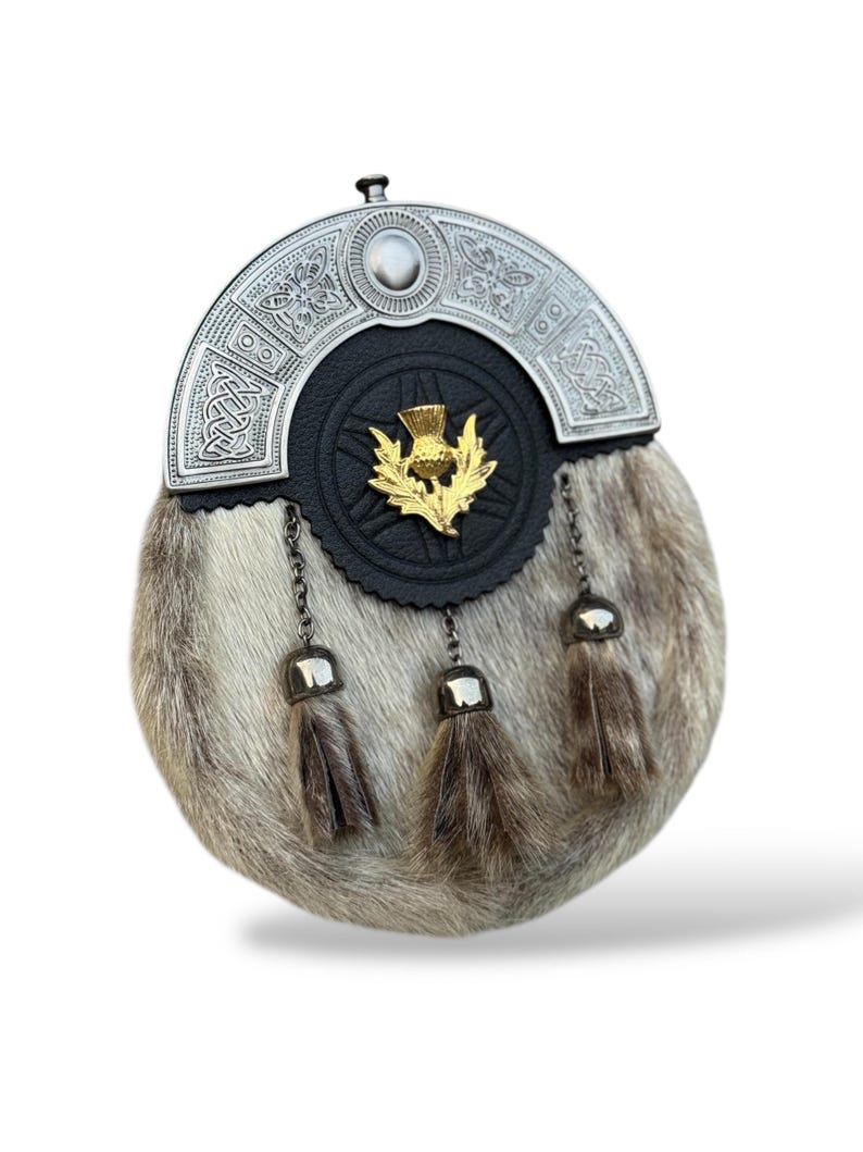 K&ouml;nnte beinhalten: Eine traditionelle schottische Sporran mit einem silbernen Cantle mit keltischen Knotenmustern und einem goldenen Distelemblem. Der Beutel ist aus Fell mit drei dekorativen Quasten und Kettendetails gefertigt.