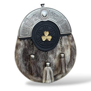 K&ouml;nnte beinhalten: Eine traditionelle schottische Sporran mit silbernem Cantle und Fellk&ouml;rper. Der Cantle zeigt keltische Knotenmuster und einen zentralen Stein. Die schwarze Lederklappe hat ein goldenes Kleeblatt-Emblem. Die Sporran hat drei Quasten mit silbernen Kappen und Ketten.
