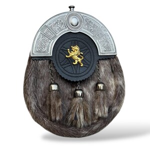 K&ouml;nnte beinhalten: Eine traditionelle schottische Sporran mit einem silbernen Cantle mit keltischen Knoten und einem zentralen Stein. Die schwarze Lederklappe hat ein goldenes L&ouml;wenemblem. Der K&ouml;rper besteht aus braunem Fell mit drei passenden Quasten.