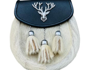 May include: A Scottish sporran with a black leather top and a silver stag head emblem. The body is made of light-coloured fur, and it has three decorative tassels with silver detailing.