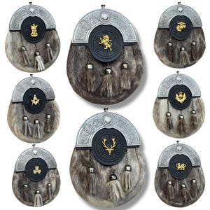Könnte beinhalten: Eine Sammlung traditioneller schottischer Sporrane, jeweils mit einem Fellkörper und einem dekorativen Metall-Cantle. Die Sporrane zeigen verschiedene Embleme, darunter einen Löwen, einen Hirsch und Freimaurersymbole, mit silberfarbenen Metallakzenten und Quasten.