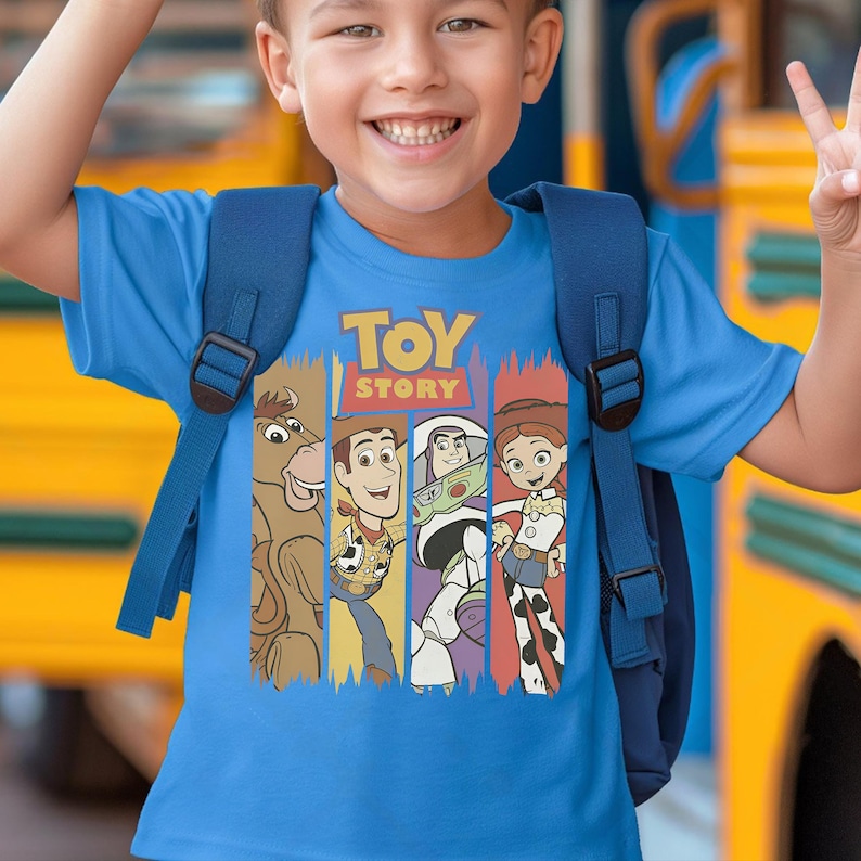 May include: A blue t-shirt featuring the words "TOY STORY" above a vertical graphic of characters from the animated film. The characters include a horse, Woody, Buzz Lightyear, and Jessie. The shirt is being worn by a child.