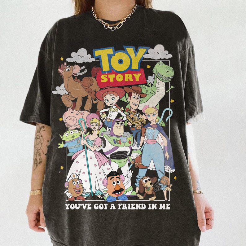 Pu&ograve; includere: T-shirt grigio scuro con una grafica colorata dei personaggi del film "Toy Story". Il design include Woody, Buzz Lightyear e altri personaggi, con le parole "TOY STORY" e "YOU'VE GOT A FRIEND IN ME."