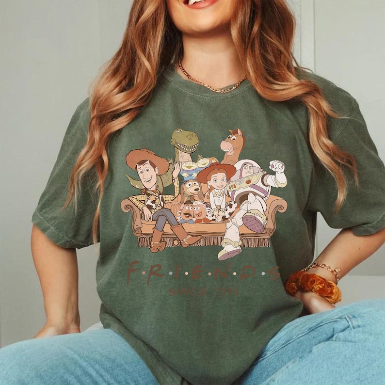 May include: Green t-shirt featuring a graphic of Toy Story characters on a couch, with the word "FRIENDS" below. The design includes Woody, Buzz Lightyear, and other characters from the animated film.