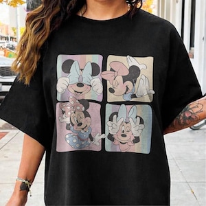 May include: Black t-shirt featuring a four-panel design of Minnie Mouse in various poses. Each panel has a pastel background with vertical stripes. Minnie is wearing different colored bows and outfits in each panel.