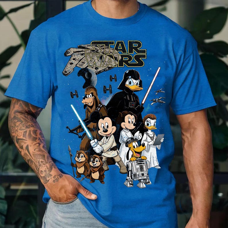 May include: Blue Star Wars t-shirt featuring a mashup of Star Wars and Disney characters. The design includes the Star Wars logo, the Millennium Falcon, Darth Vader, Mickey Mouse, Donald Duck, and other characters with lightsabers.