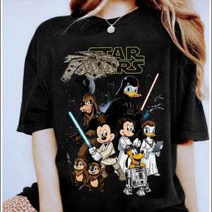 May include: Black t-shirt featuring a Star Wars graphic with Disney characters. The design includes Mickey Mouse, Minnie Mouse, Donald Duck, Daisy Duck, Goofy, Pluto, Chip and Dale, and R2-D2, with a Star Wars logo.