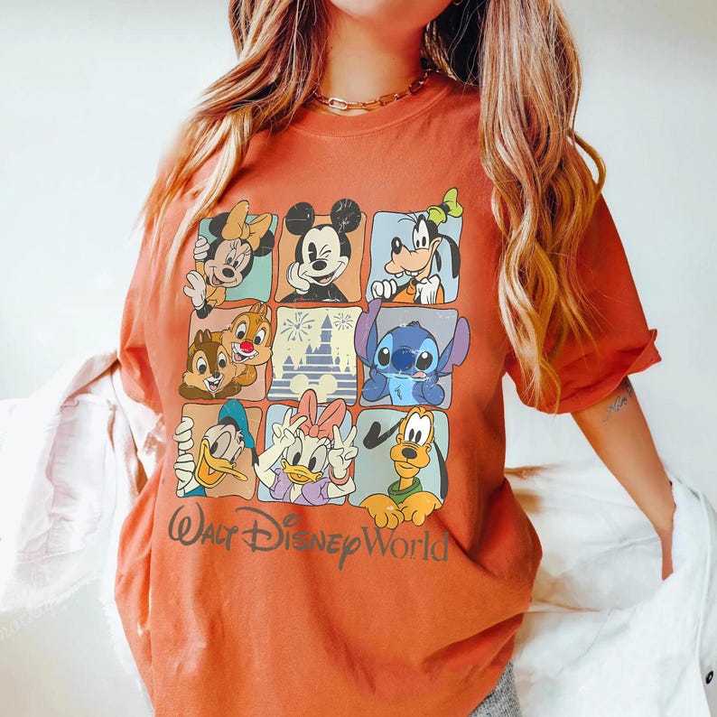 Puede incluir: Camiseta naranja quemado con una cuadr&iacute;cula de personajes de Disney, incluyendo Mickey Mouse, Minnie Mouse, Goofy, Chip y Chop, Stitch, Donald Duck y Daisy Duck. Las palabras "Walt Disney World" est&aacute;n impresas en cursiva.