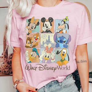 Puede incluir: Camiseta rosa claro con una cuadr&iacute;cula de personajes de Disney, incluyendo Mickey y Minnie Mouse, Donald y Daisy, Goofy, Pluto, Chip y Chop, y Stitch. Las palabras "Walt Disney World" est&aacute;n impresas debajo.