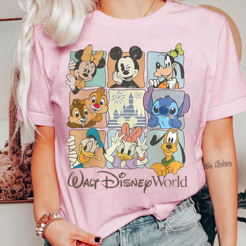 Puede incluir: Camiseta rosa claro con una cuadr&iacute;cula de personajes de Disney, incluyendo Mickey y Minnie Mouse, Donald y Daisy, Goofy, Pluto, Chip y Chop, y Stitch. Las palabras "Walt Disney World" est&aacute;n impresas debajo.