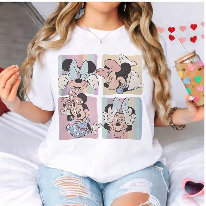 May include: White t-shirt featuring a four-panel design of Minnie Mouse in various poses. Each panel has a pastel striped background. Minnie is wearing different bows and outfits. The shirt is paired with light blue jeans.