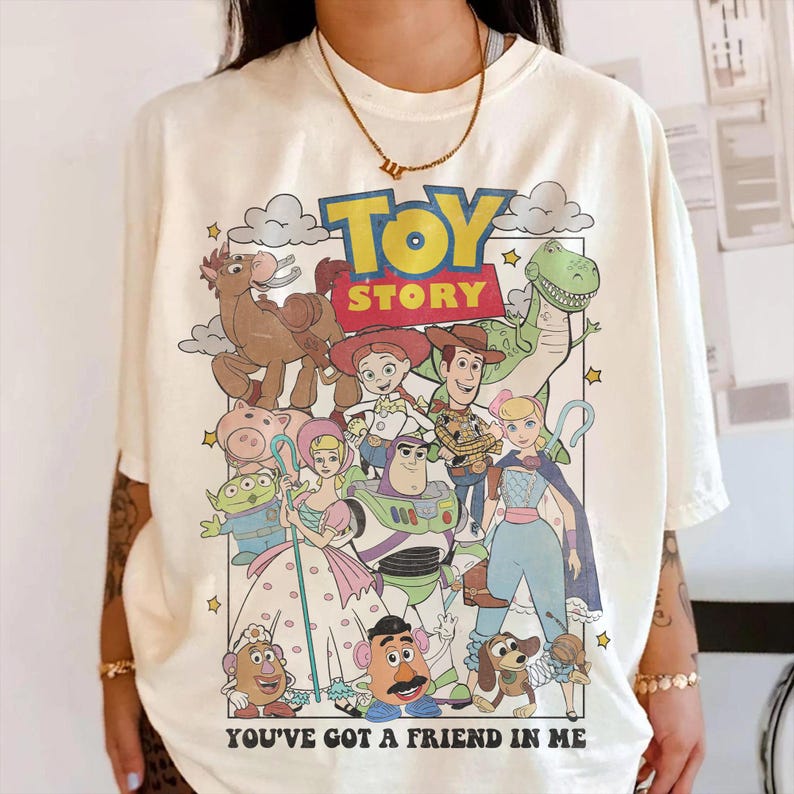 Pu&ograve; includere: T-shirt color crema con una grafica colorata dei personaggi del film d'animazione "Toy Story". Il design include il logo del film e la frase "You've Got a Friend in Me".