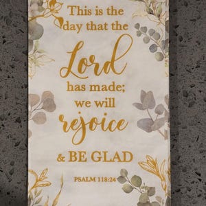 May include: A white rectangular decorative item with gold lettering that reads "This is the day that the Lord has made; we will rejoice & BE GLAD" and "PSALM 118:24". The item is decorated with green and gold floral accents.