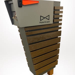 May include: A contemporary mailbox with a grey metal body and a slatted wooden front. The mailbox has a bright orange flag and the "MakerScape" logo. It is supported by two wooden posts.