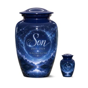 Puede incluir: Una urna funeraria grande y una pequeña de color azul oscuro con un diseño de cielo nocturno celestial, montañas, un lago y estrellas. El texto Son, 2005-2024 y The Stars Know Your Name aparece en letras blancas en ambas urnas.