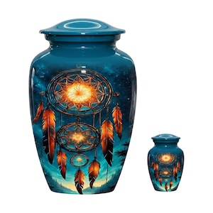 Puede incluir: Una urna funeraria grande y una pequeña de color verde azulado, cada una con un diseño impreso de tres atrapasueños apilados con centros de color naranja brillante y plumas colgantes sobre un cielo estrellado azul oscuro.