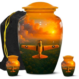 May include: A set of three urns with a sunset and airplane design. The large urn has a lid and a black drawstring bag. The urns are orange with a sunset scene and a yellow airplane.
