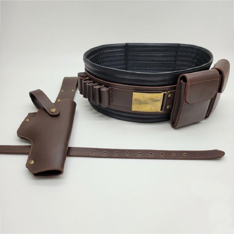 Puede incluir: Un cintur&oacute;n utilitario marr&oacute;n oscuro con forro interior negro, una hebilla rectangular color lat&oacute;n, m&uacute;ltiples trabillas integradas y bolsillos de almacenamiento. Una funda marr&oacute;n a juego con una correa larga se sit&uacute;a a la izquierda.