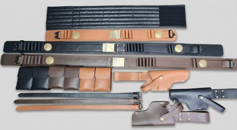 Puede incluir: Una colecci&oacute;n de art&iacute;culos de cuero que incluye varios cinturones con cartucheras y emblemas circulares dorados, bolsas rectangulares en negro, marr&oacute;n y tostado, tres cinturones de cuero lisos y dos fundas de cuero en color tostado y negro.