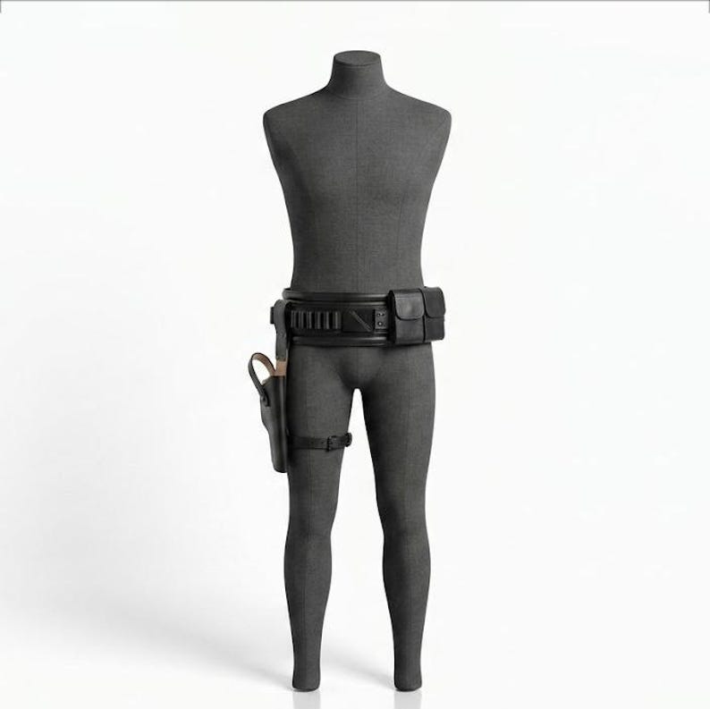 Puede incluir: Un cintur&oacute;n utilitario negro sobre un torso de maniqu&iacute; gris oscuro. El cintur&oacute;n presenta una serie de bolsillos rectangulares, una funda r&iacute;gida unida al lado derecho y una correa fina para la pierna. El dise&ntilde;o incluye compartimentos.