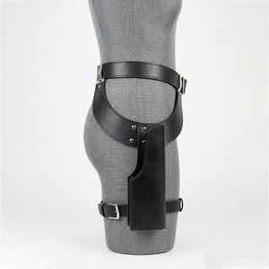May include: A black leather thigh holster belt featuring a wide waist strap, a vertical holster pouch attached with silver-toned metal rivets, and a secondary adjustable leg strap with a metal buckle, all displayed on a gray mannequin torso.