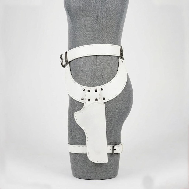 Op de afbeelding: Een witte lederen dijbeenholsterriem met een brede tailleband, een gebogen heuppaneel vastgezet met zilverkleurige metalen klinknagels en een verticale holsterzak. Het geheel bevat een verstelbare beenband met een zilverkleurige metalen gesp.
