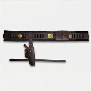 Puede incluir: Un cintur&oacute;n utilitario de cuero marr&oacute;n oscuro que incluye una funda, dos bolsas de almacenamiento y m&uacute;ltiples bucles para munici&oacute;n. El cintur&oacute;n cuenta con una hebilla rectangular de lat&oacute;n, dos emblemas circulares de lat&oacute;n y una correa de pierna.