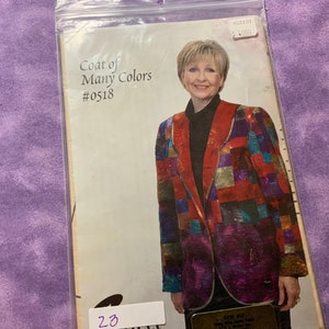 May include: A sewing pattern titled "Coat of Many Colors" featuring a woman wearing a colorful patchwork jacket. The jacket has a red collar and is made of squares in shades of red, blue, green, and purple. The pattern number is #0518.