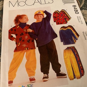 May include: McCall's sewing pattern 8480 featuring children's clothing. The pattern shows a boy and girl wearing outfits. The outfits include tops and pants in various colors and patterns. The pattern is for size 5-6.