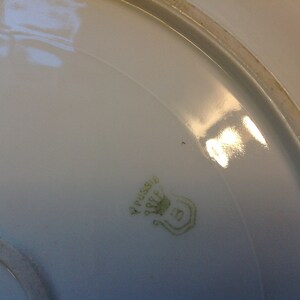 Puede incluir: Primer plano de la parte inferior de un plato de porcelana blanca con una marca verde que dice "V. Pussiere" y una corona con el n&uacute;mero "5" debajo.