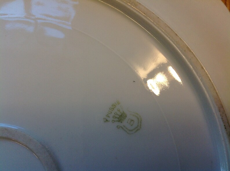 Puede incluir: Primer plano de la parte inferior de un plato de porcelana blanca con una marca verde que dice "V. Pussiere" y una corona con el n&uacute;mero "5" debajo.