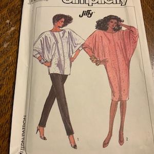 May include: A sewing pattern for a Jiffy brand dress with two different styles. The first style is a white top with long sleeves and black pants. The second style is a pink dress with long sleeves. The pattern is labeled "Simplicity".