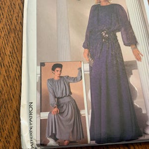 May include: A vintage sewing pattern for a long, flowing dress with a gathered skirt and long sleeves. The pattern is for sizes 6-14 and includes instructions for making the dress.