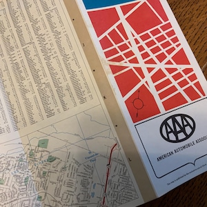 May include: Open vintage map with a red and white street grid design and the AAA logo. The map includes a detailed street directory and a section of a city map, ideal for navigation and travel.