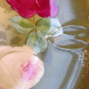Puede incluir: Un plato de porcelana vintage con fondo verde y dise&ntilde;o floral. El plato presenta una rosa rosa y blanca con hojas verdes y un borde dorado.